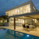 A pool and patio area with chairs, table and lights.